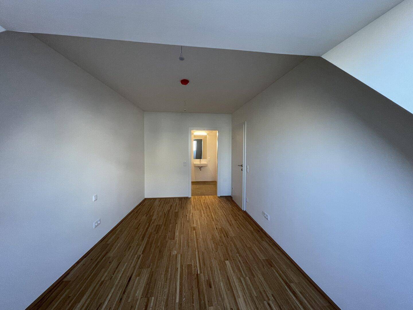 Leeres Schlafzimmer mit Holzboden und Zugang zu einem modernen Badezimmer, ideal für individuelle Gestaltung.