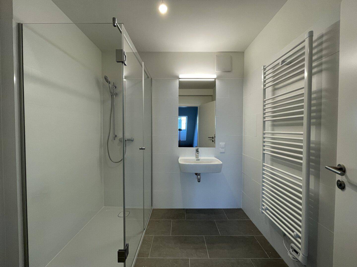 Modernes Badezimmer mit ebenerdiger Dusche, Einzelwaschbecken und beheiztem Handtuchhalter, in hellen Farben gehalten.