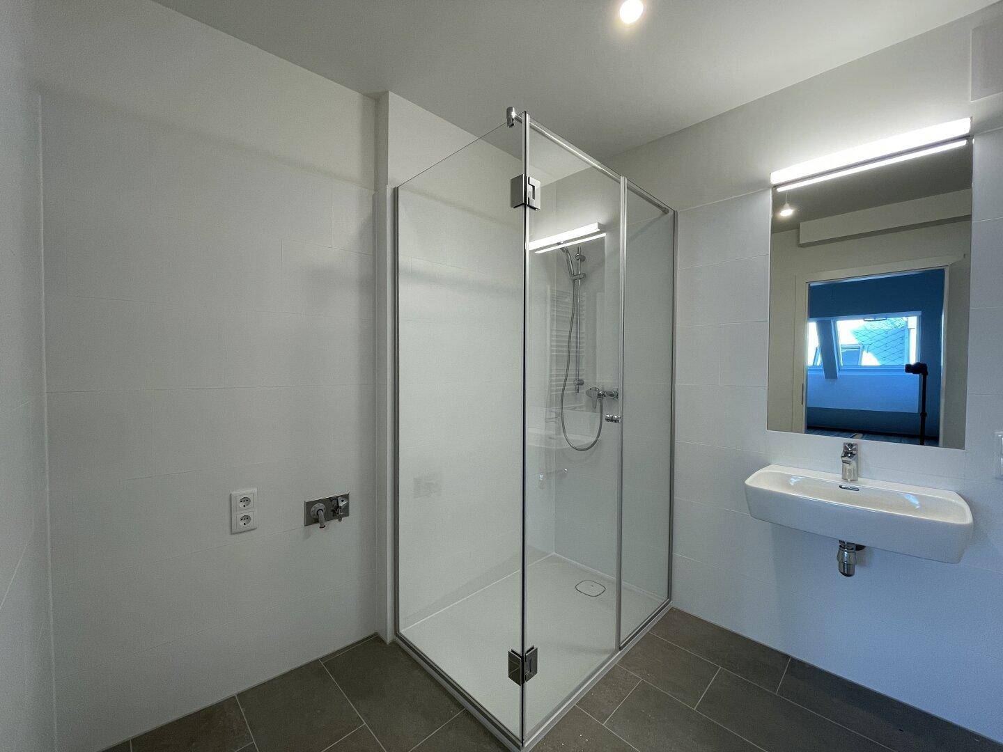 Zeitgemäßes Badezimmer mit geräumiger Glasdusche, Einzelwaschbecken und Fliesenboden, sehr gepflegt.