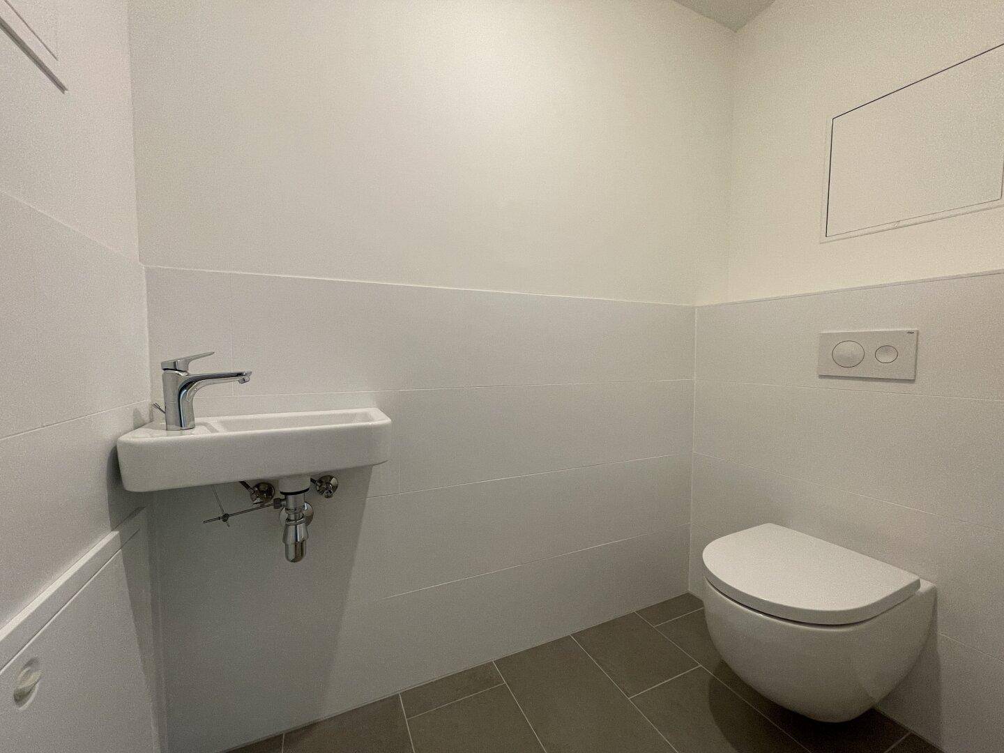 Modernes Gäste-WC mit wandhängender Toilette und kleinem Waschbecken, in schlichtem Design gehalten.