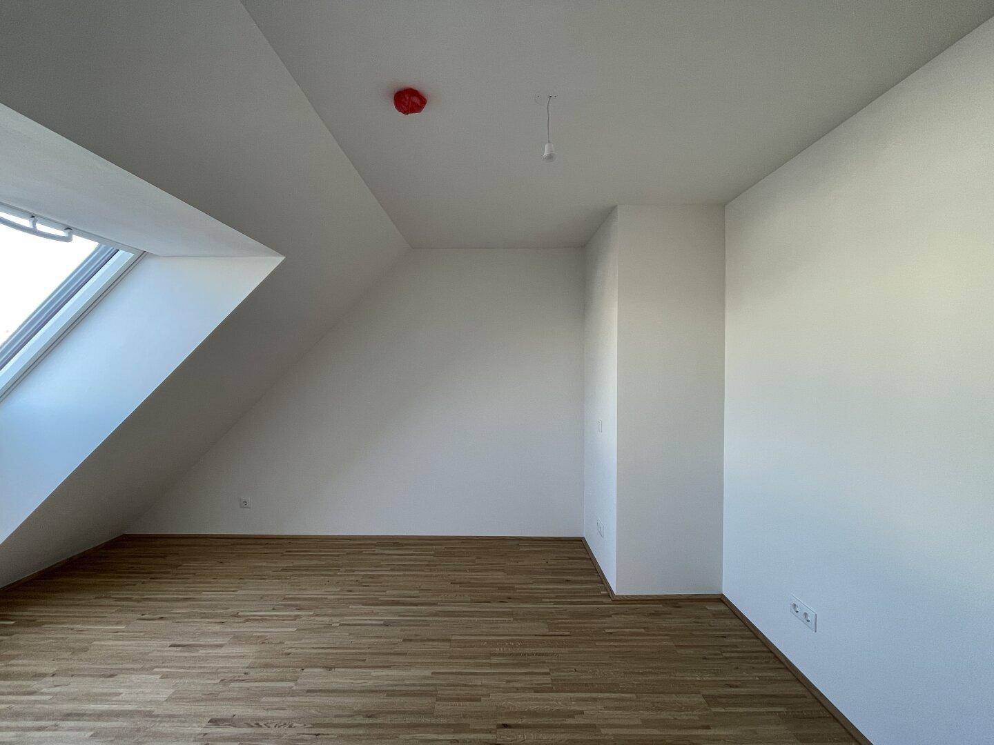 Geräumiges Zimmer im Dachgeschoss mit Parkettboden, Dachschräge und viel Tageslicht.