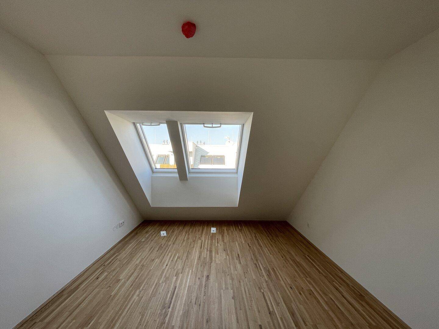 Helles Zimmer im Dachgeschoss mit Parkettboden und zwei großen Dachfenstern.