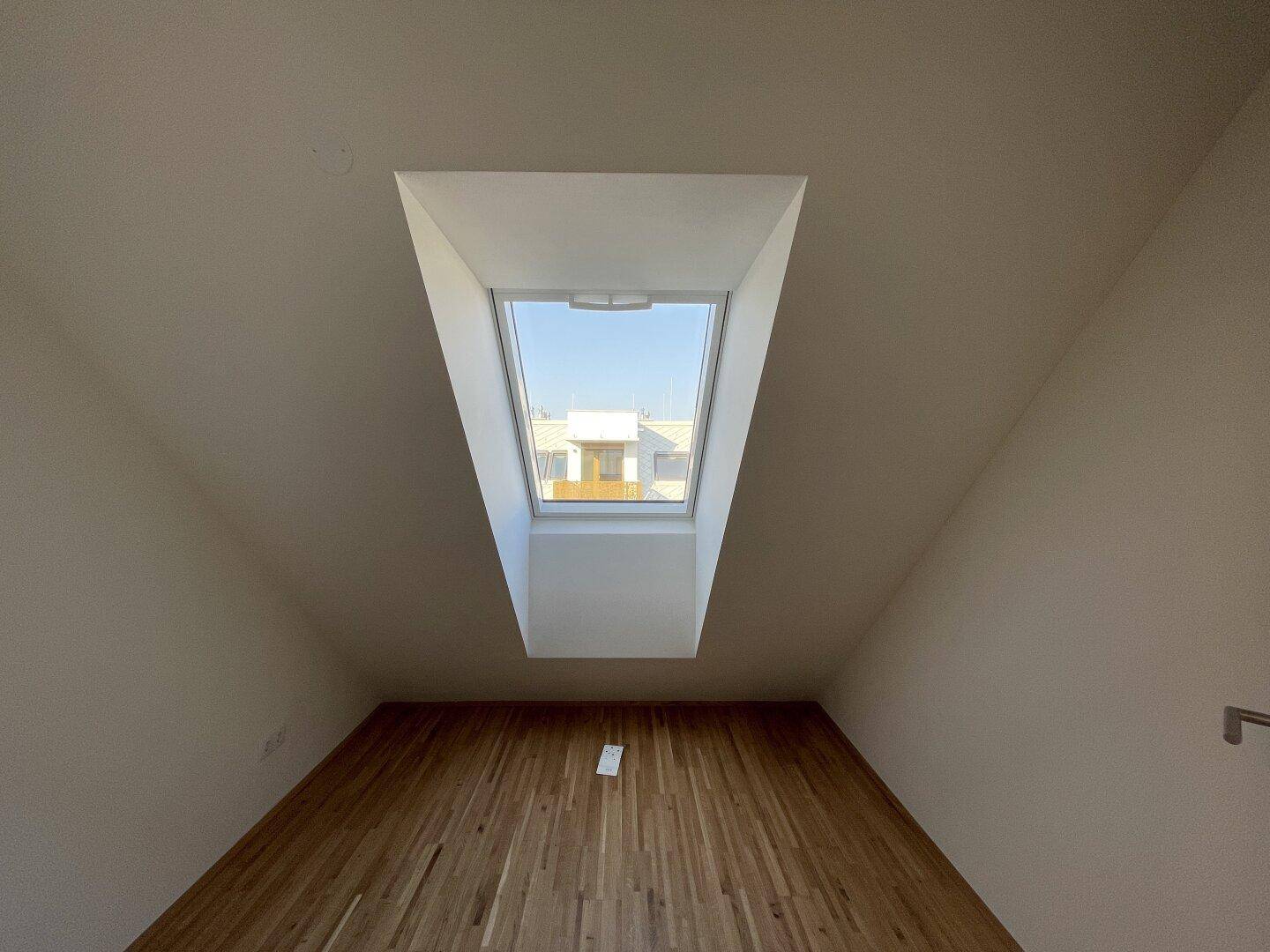 Helles Zimmer im Dachgeschoss mit Parkettboden und einem großen Dachfenster.