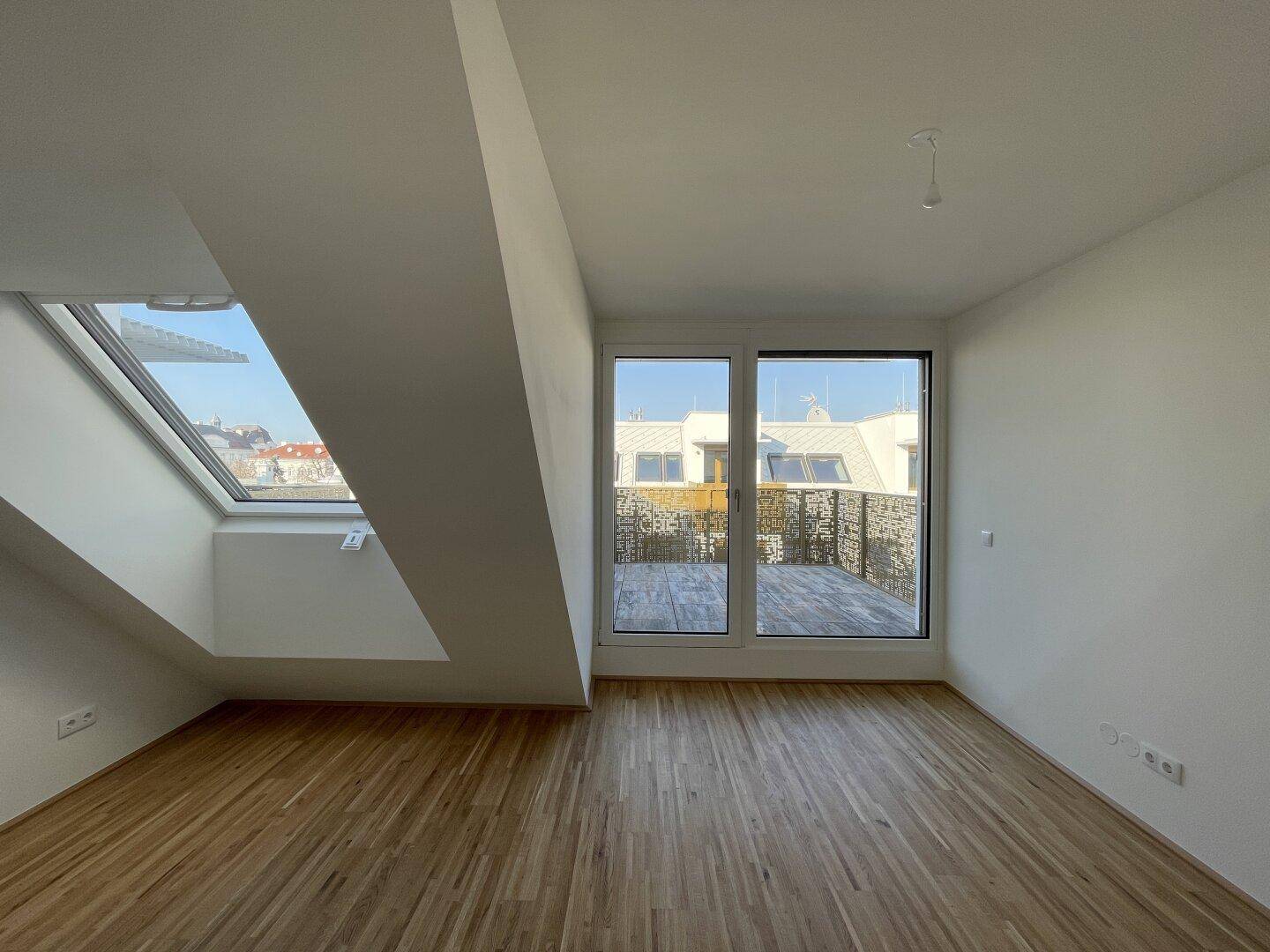 Helles Dachgeschosszimmer mit Holzboden, Dachfenster und Zugang zu einer Terrasse.