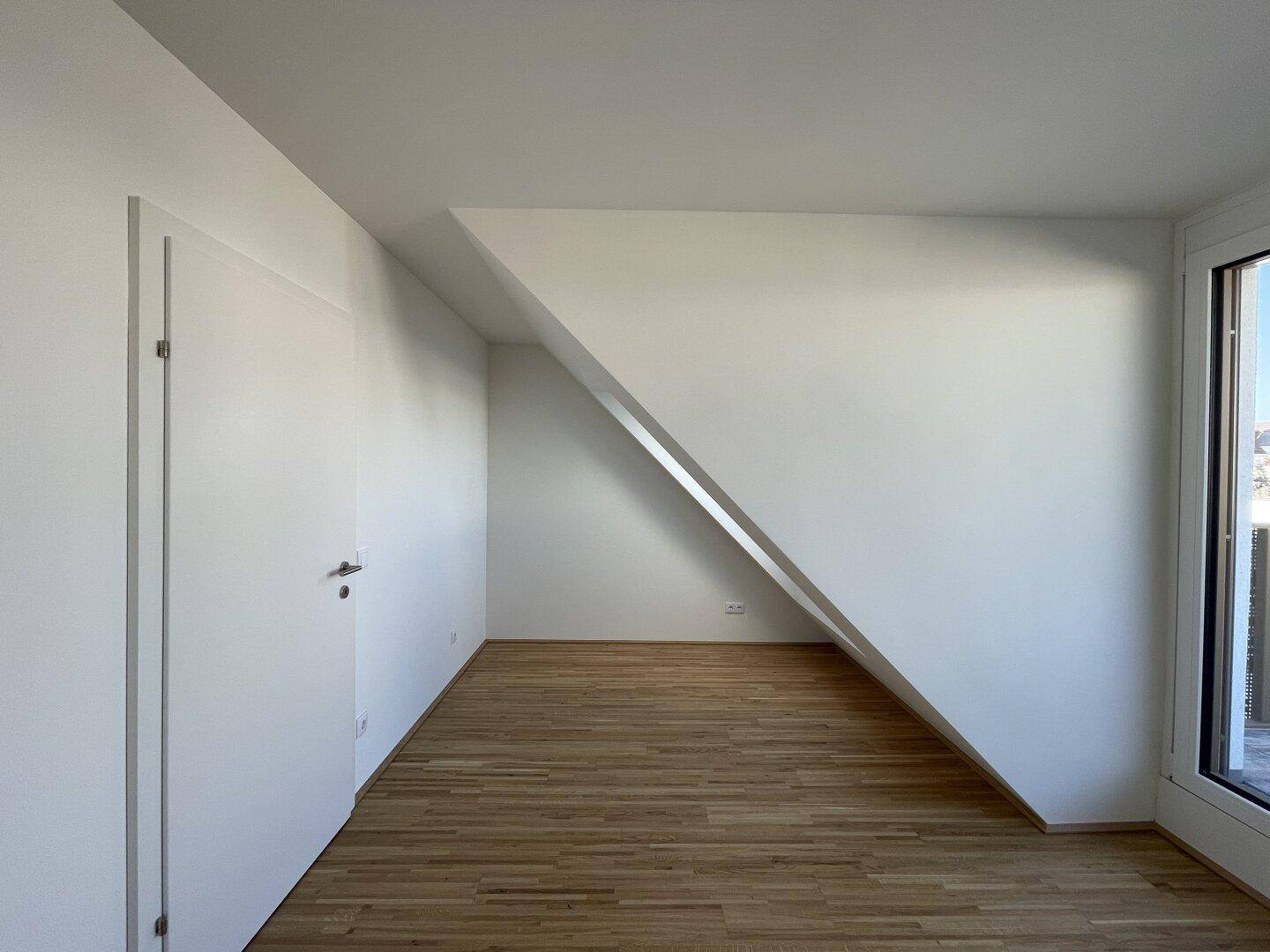 Unmöblierter Raum im Dachgeschoss mit Holzboden und schräger Wand.
