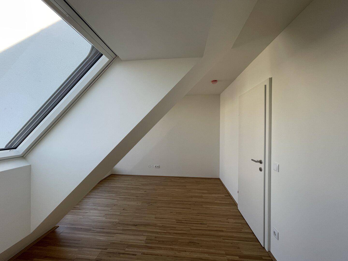 Dachgeschosszimmer mit Holzboden, schräger Wand und einem Dachfenster.