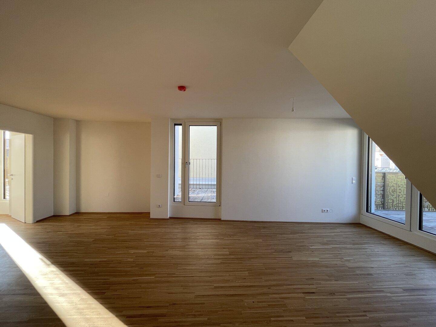 Geräumiger Wohnbereich mit hellem Parkettboden und großen Fenstern zum Außenbereich.
