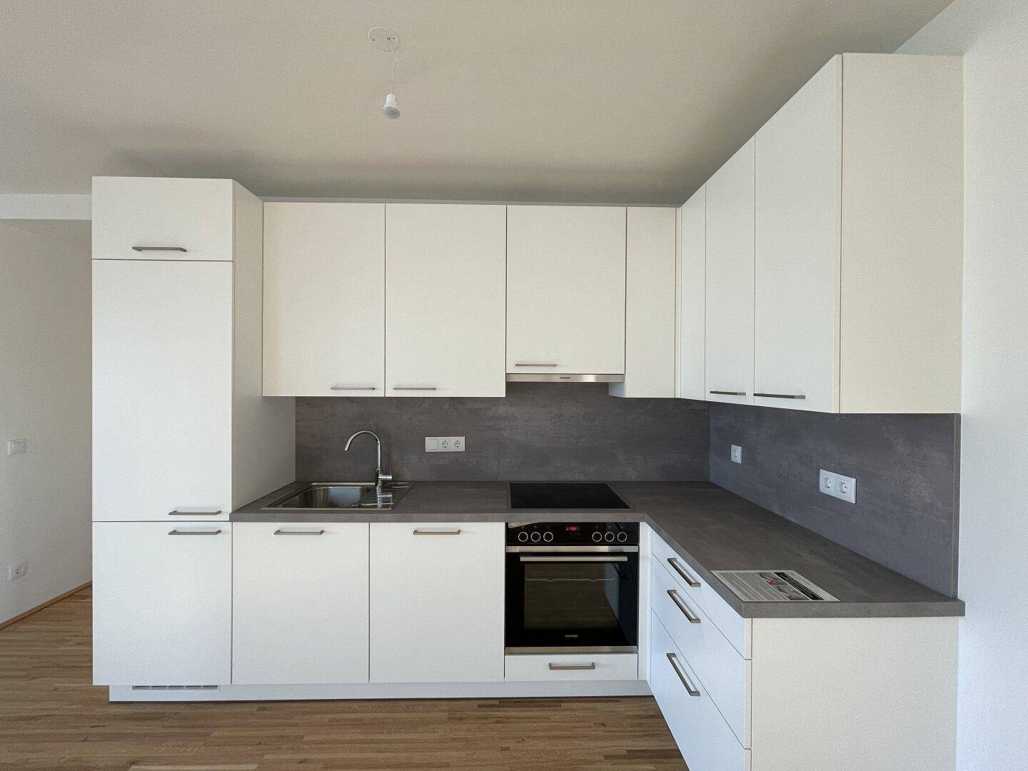 Moderne Einbauküche mit weißen Schränken, dunkler Arbeitsplatte und integrierten Geräten.