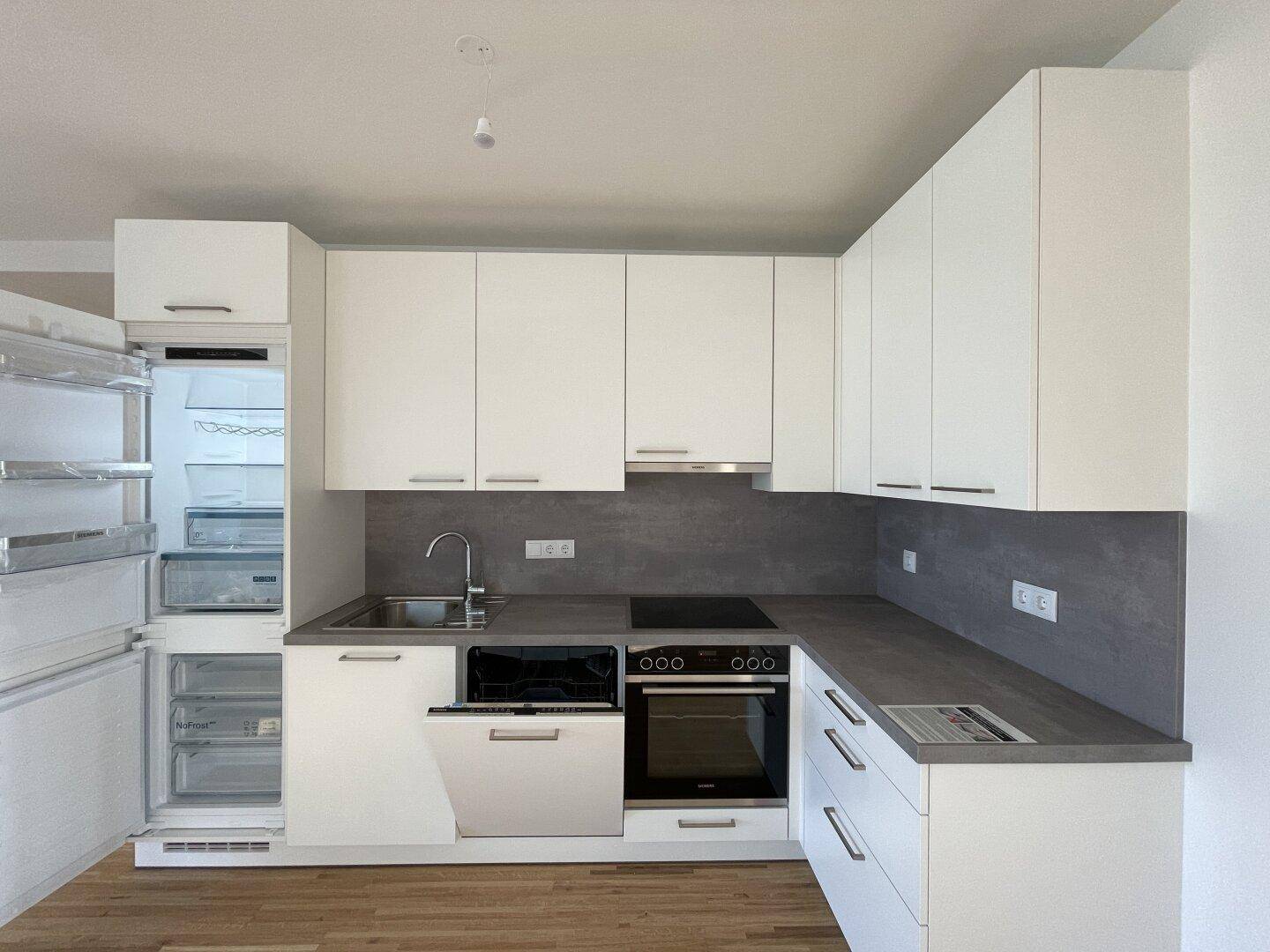 Voll ausgestattete moderne Küche mit weißen Fronten, Kühlschrank und Geschirrspüler.