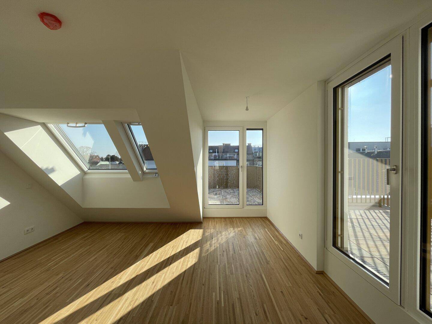 Helles Schlafzimmer im Dachgeschoss mit Parkettboden, Dachfenstern und Terrassenzugang.