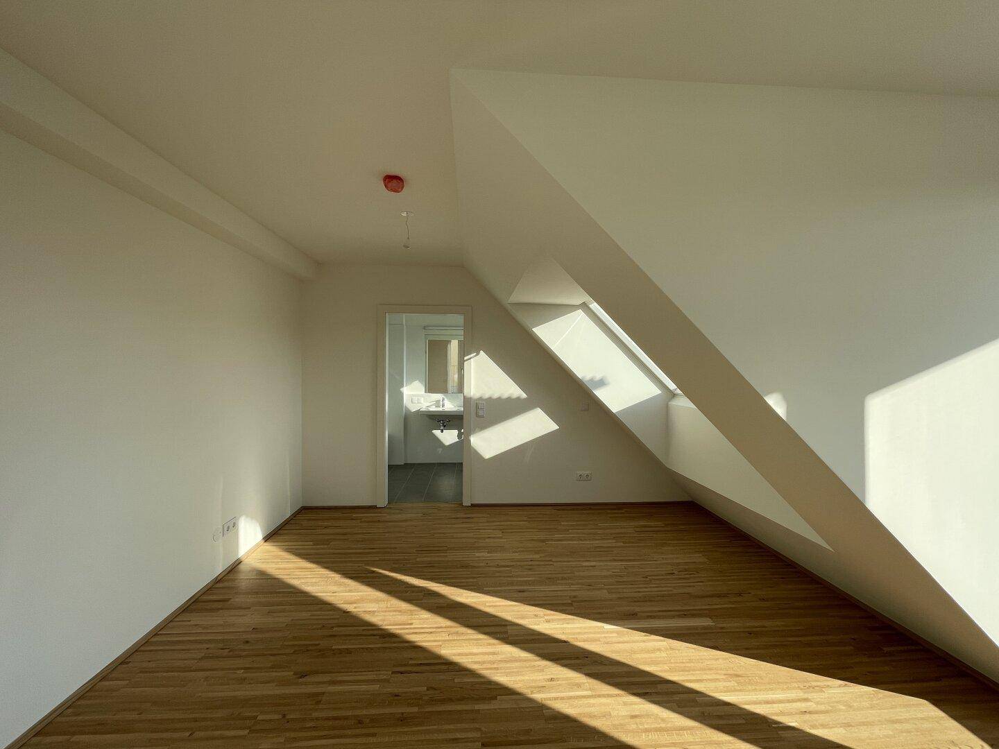 Geräumiges Schlafzimmer mit Parkettboden, Dachschrägen und angrenzendem Badezimmer.