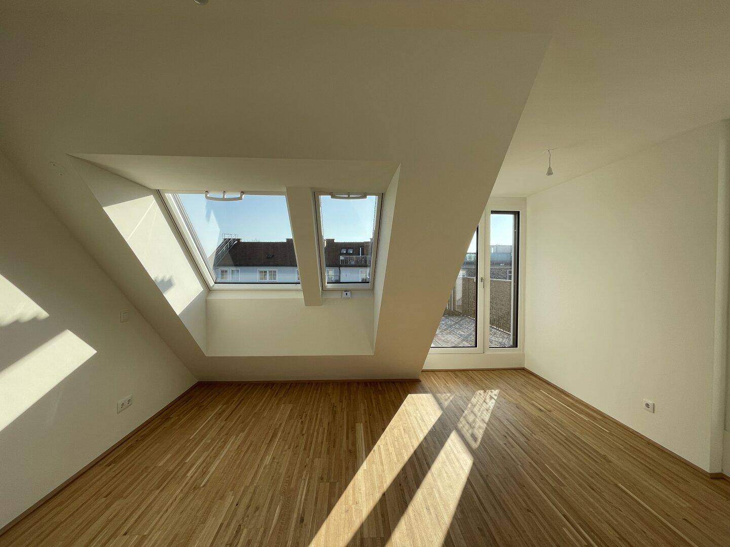 Helles Schlafzimmer mit Parkettboden, Dachfenstern und direktem Zugang zur Terrasse.
