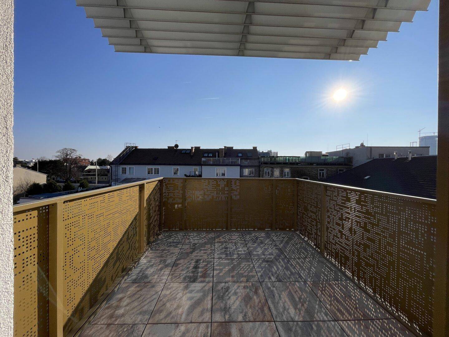 Sonnige Dachterrasse mit modernen Fliesen, perforiertem Geländer und weitem Stadtblick.