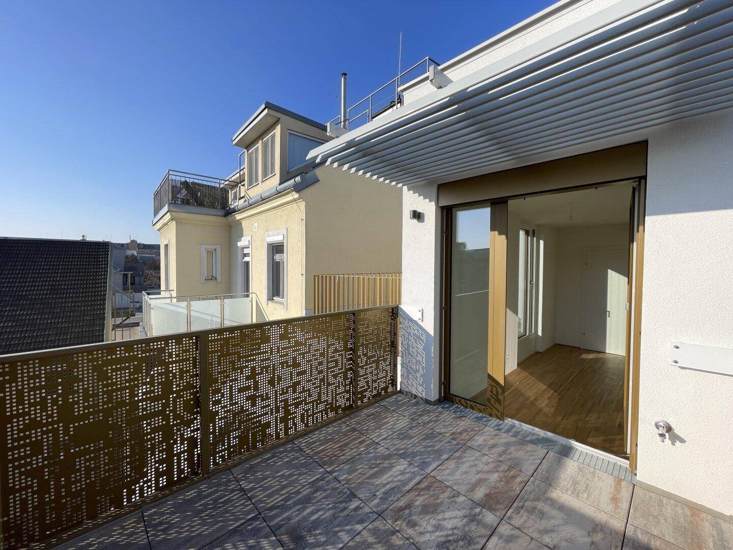 Moderne Dachterrasse mit Fliesenboden, perforiertem Geländer und Zugang zum Innenbereich.