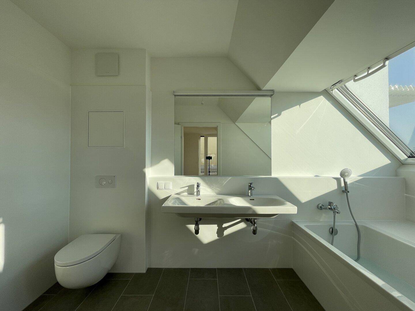 Modernes Badezimmer mit Doppelwaschbecken, Badewanne und Tageslicht durch Dachfenster.