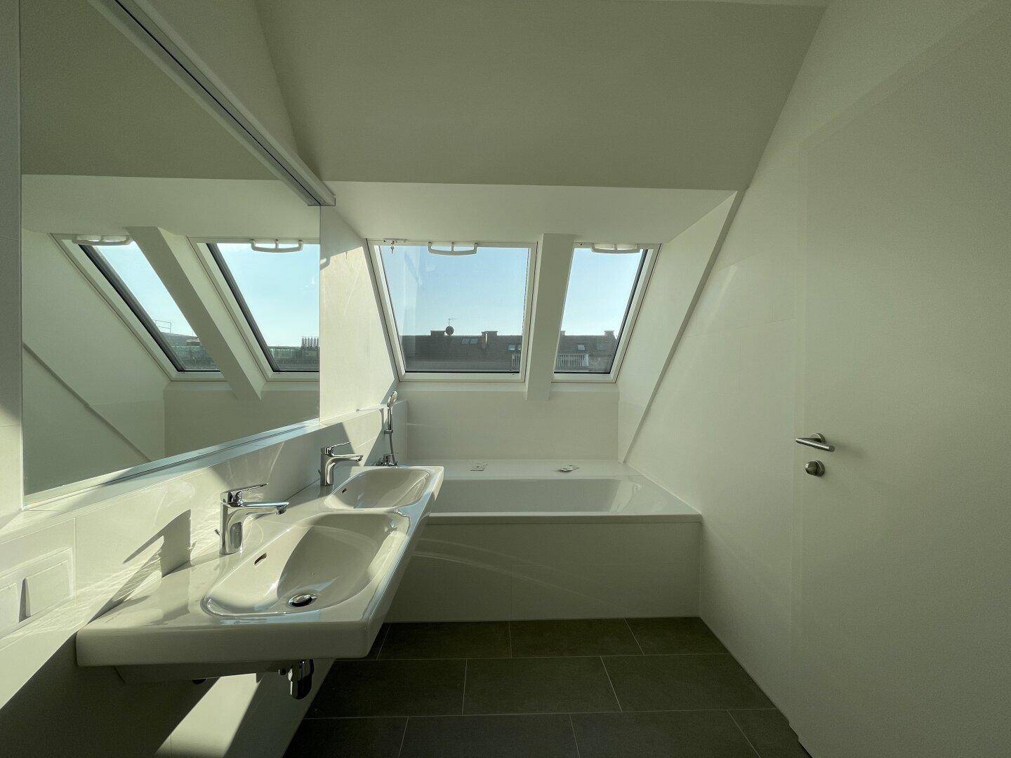 Helles Badezimmer mit Doppelwaschbecken, Badewanne und schrägen Wänden im Dachgeschoss.
