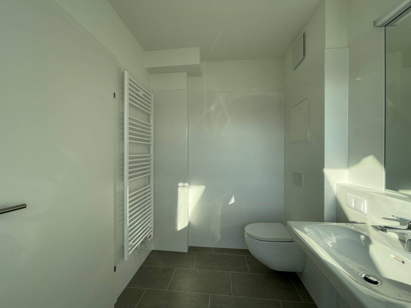 Modernes Badezimmer mit wandhängendem WC, Waschbecken und beheiztem Handtuchhalter.