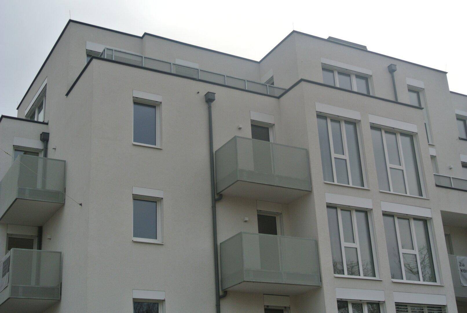 Moderne Gebäudefassade mit mehreren Balkonen und großen Fenstern, typisch für Neubauten.