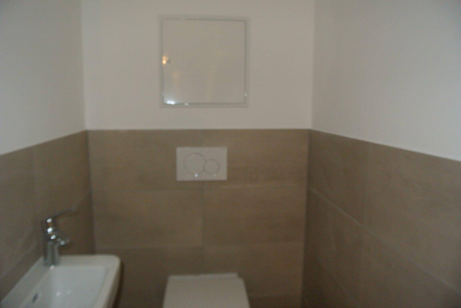 Kleines Gäste-WC mit Wand-WC, kleinem Waschbecken und beigefarbenen Fliesen.