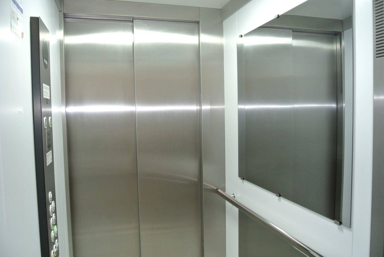 Moderner Aufzug mit Edelstahltüren und einem Spiegel im Innenraum.