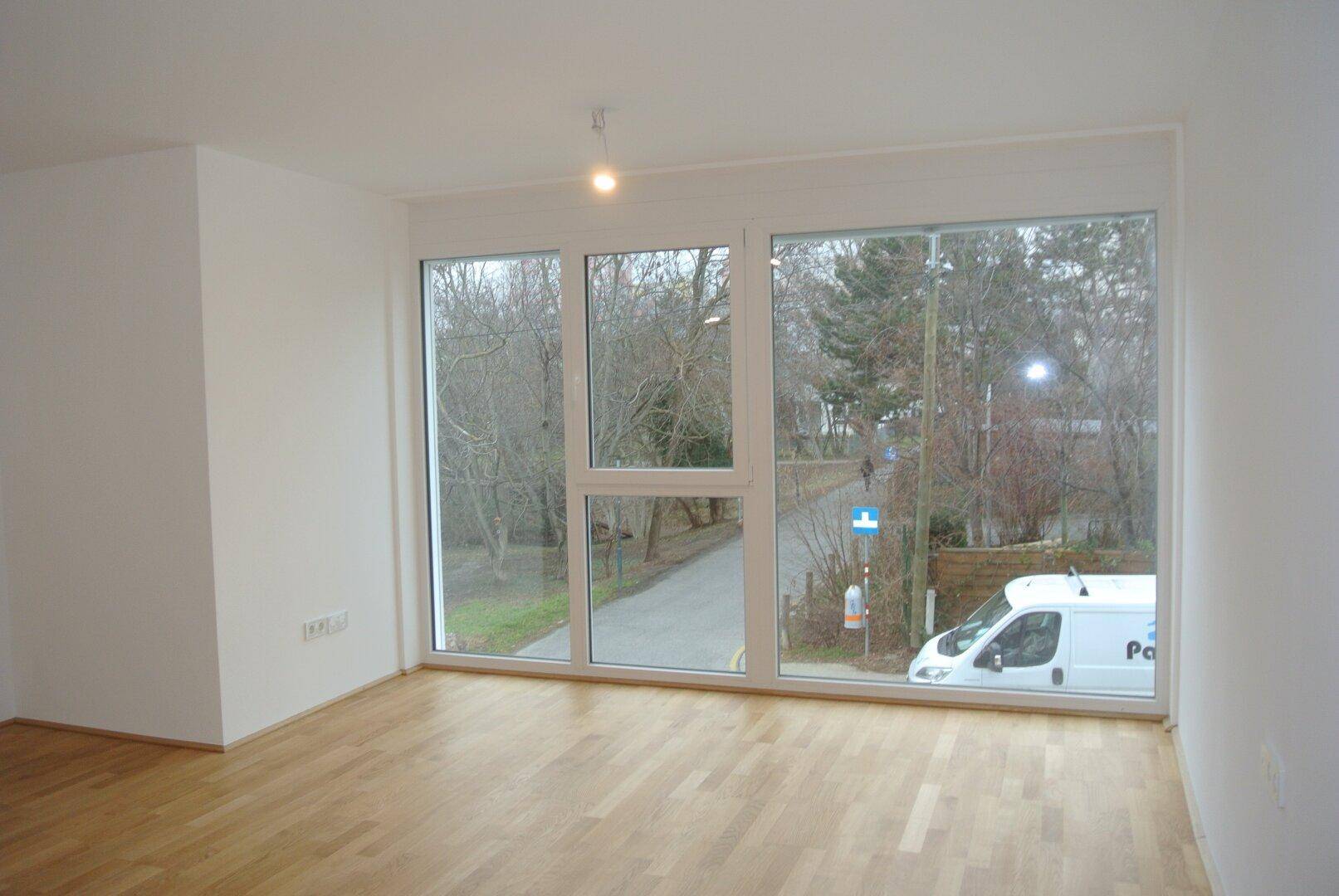 Heller, leerer Raum mit großen Fenstern und Holzboden, Blick auf die Straße.