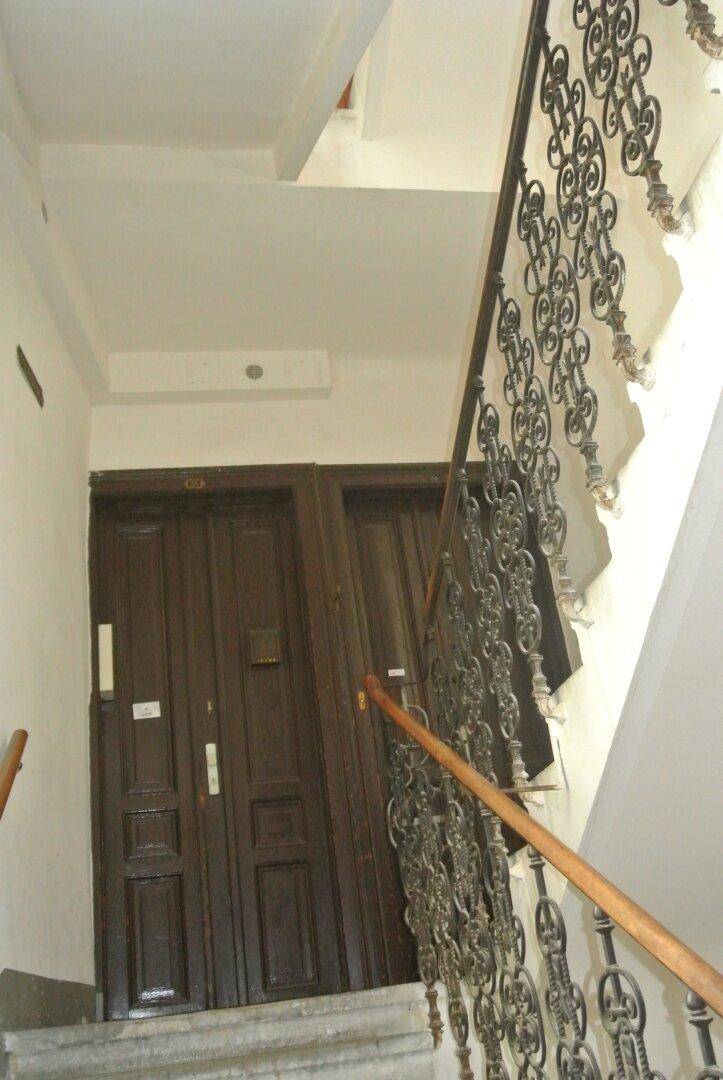 Historisches Treppenhaus mit schmiedeeisernem Geländer und dunklen Holztüren zu den Wohnungen.