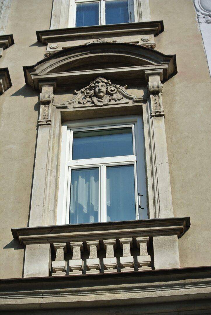 Detailansicht eines reich verzierten Fensters mit Balustrade an der historischen Fassade des Gebäudes.