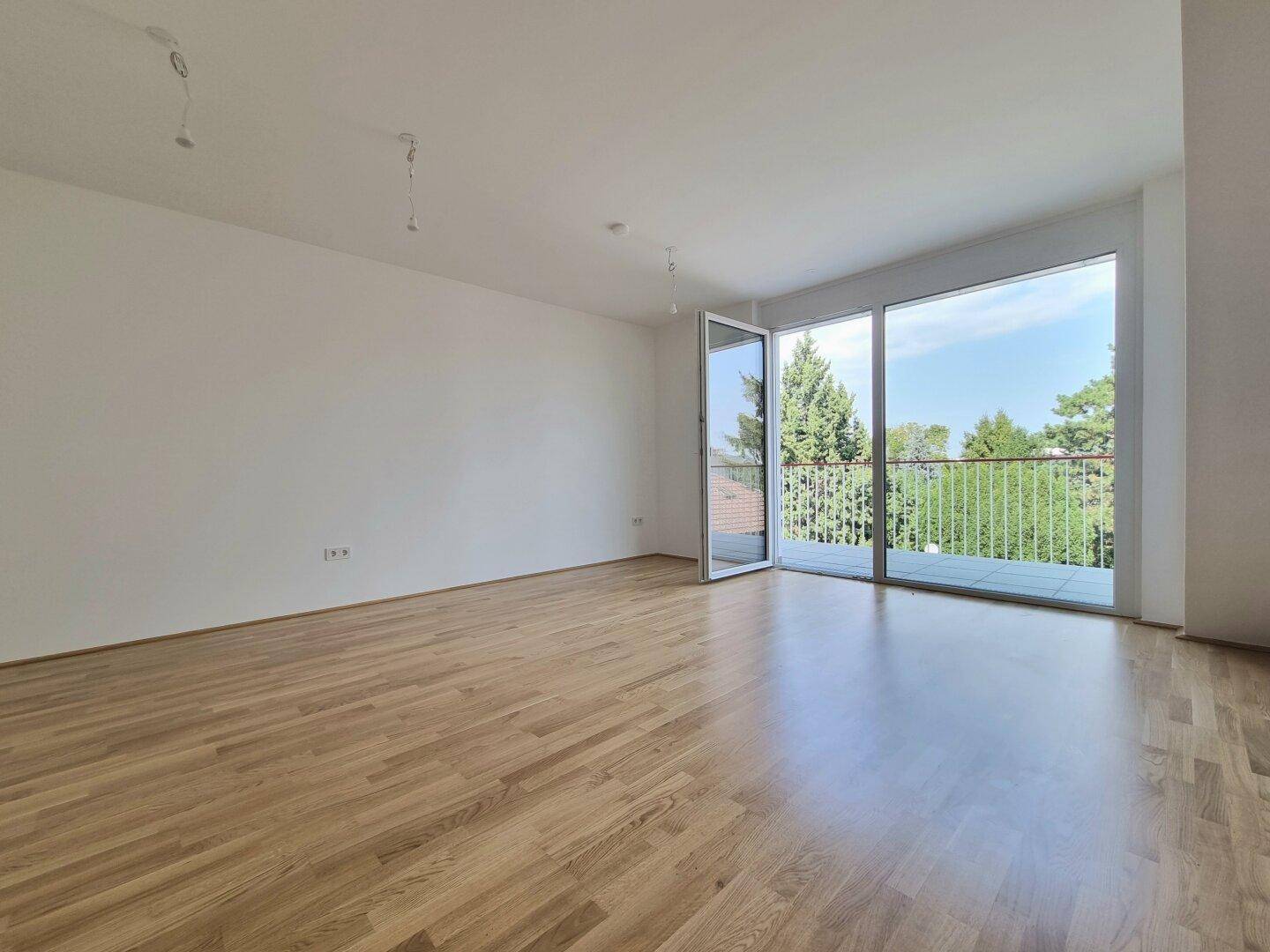 Helles Wohnzimmer mit Holzboden und großen Fenstern, die Zugang zu einem Balkon bieten.