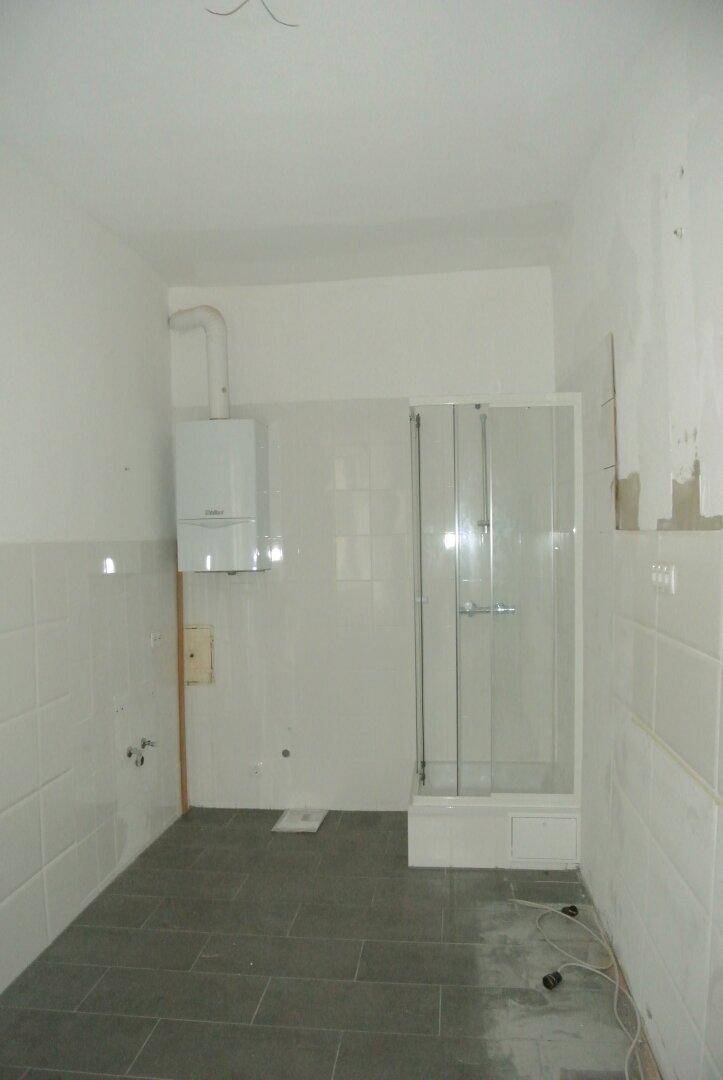 Badezimmer im Rohzustand mit Duschkabine, Wandfliesen und Gastherme, renovierungsbedürftig.