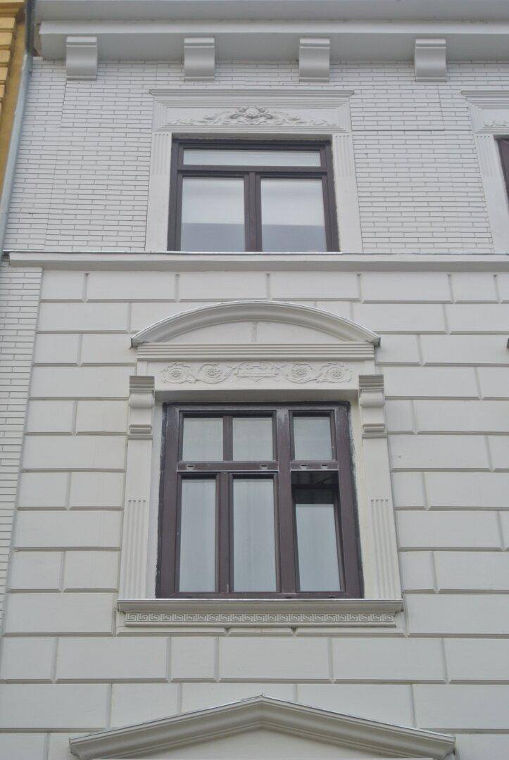 Nahaufnahme der weißen Fassade mit strukturiertem Putz und einem verzierten Fensterrahmen.