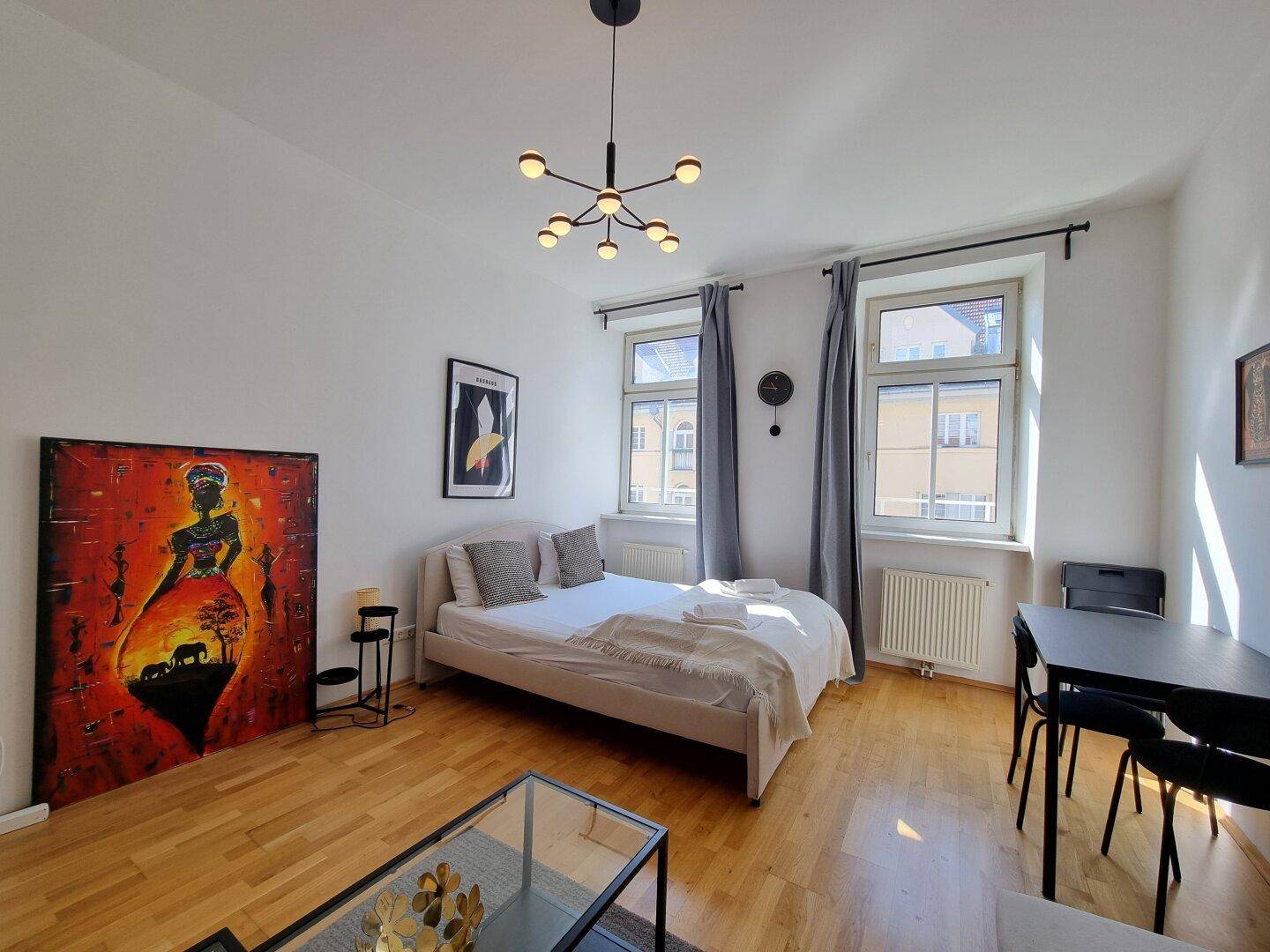 Gemütliches Studio-Apartment mit Holzboden, Bett, Sofa und moderner Beleuchtung, hell und einladend.