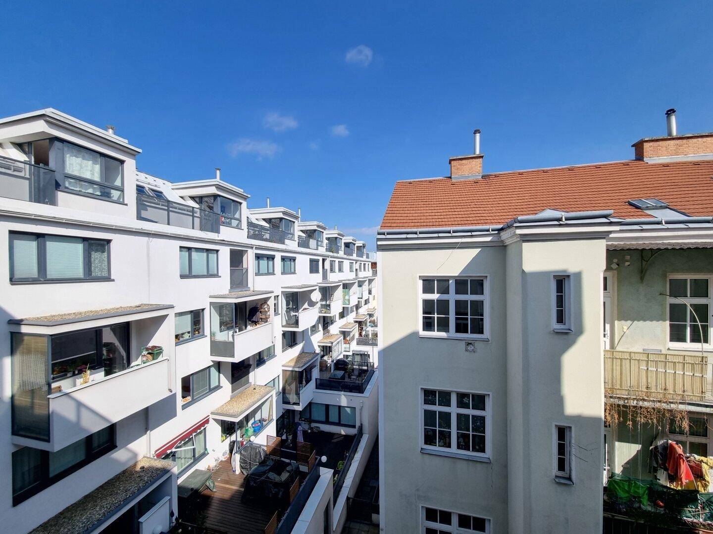 Blick auf benachbarte Gebäude mit zahlreichen Balkonen und Dachterrassen unter blauem Himmel.