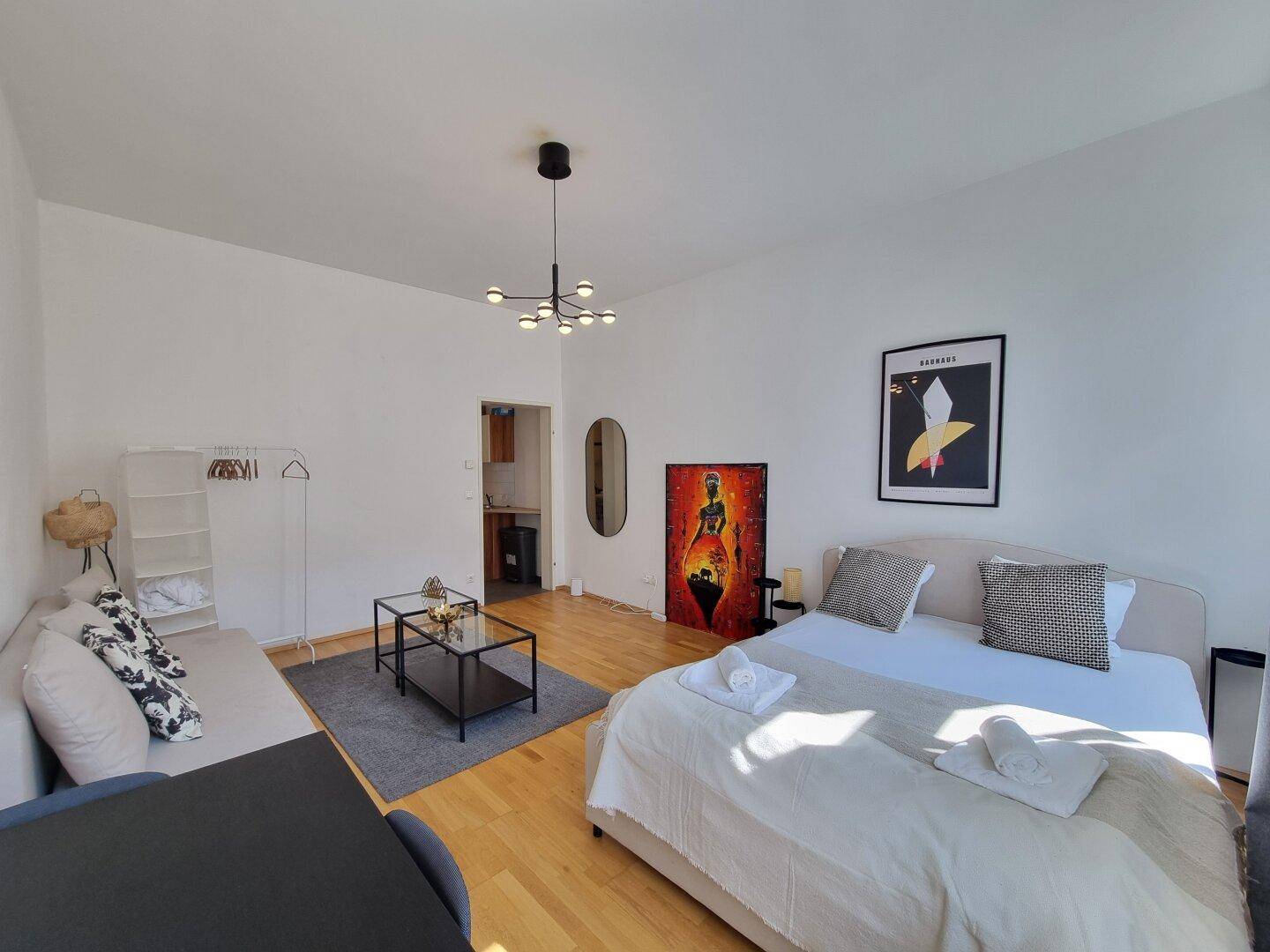 Studio-Wohnbereich mit Holzboden, Schlafsofa und Blick auf den Kücheneingang, modern eingerichtet.