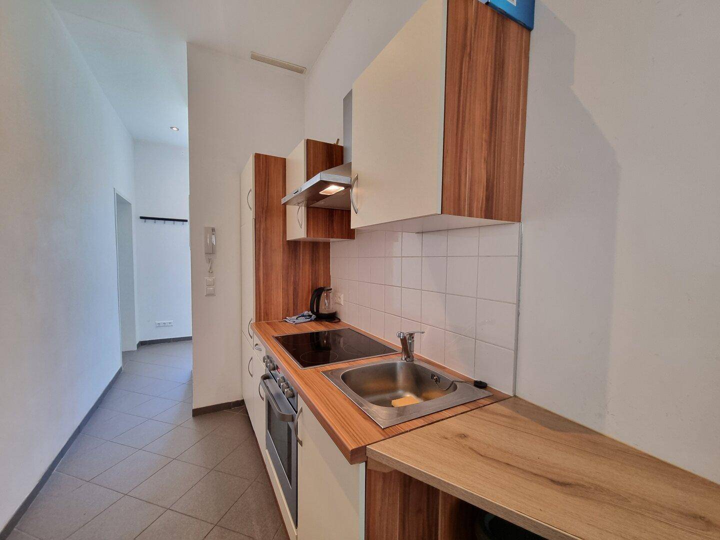 Kleine Küchenzeile mit Holz-Arbeitsplatte, Kochfeld und Spüle in hellem Design, funktional und kompakt.