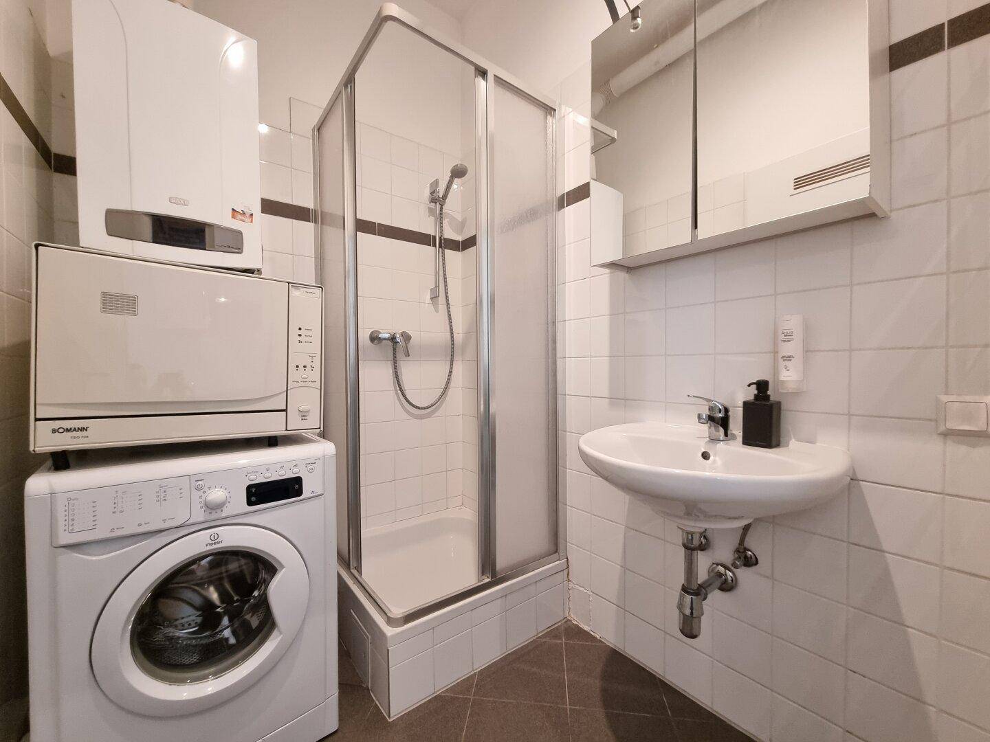 Badezimmer mit Duschkabine, Waschbecken, Waschmaschine und Boiler, praktisch und hell gefliest.