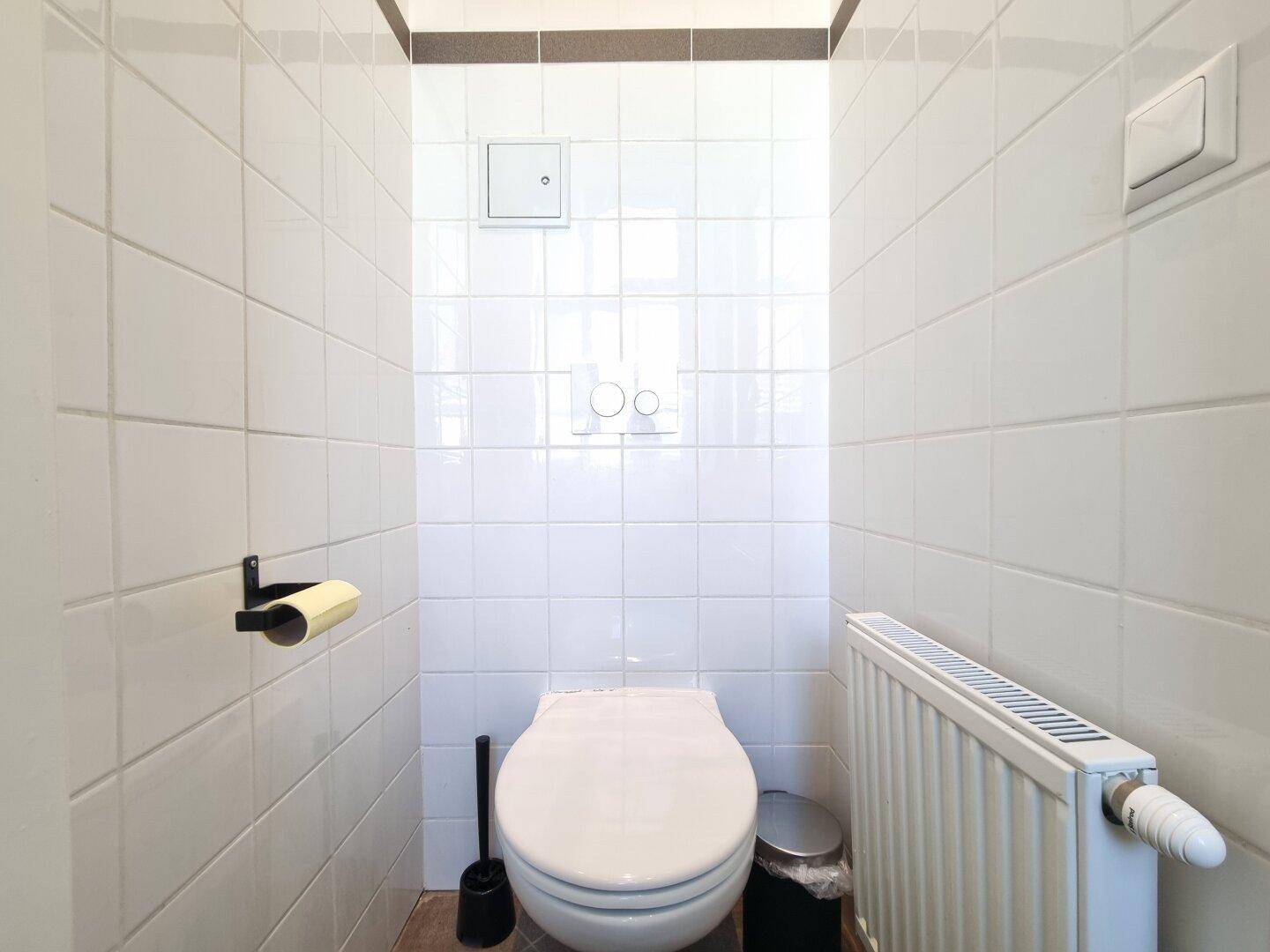 Separates WC mit weißen Fliesen, Toilette und Heizkörper, sauber und funktional gestaltet.