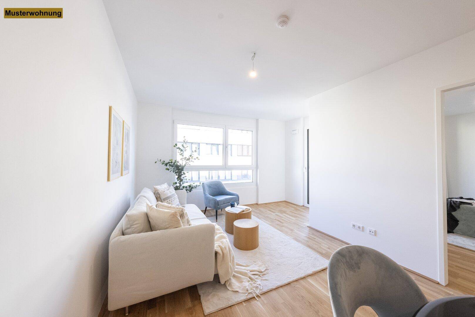 Gemütlicher Wohnbereich mit hellem Sofa, blauem Sessel und großen Fenstern für viel Tageslicht.