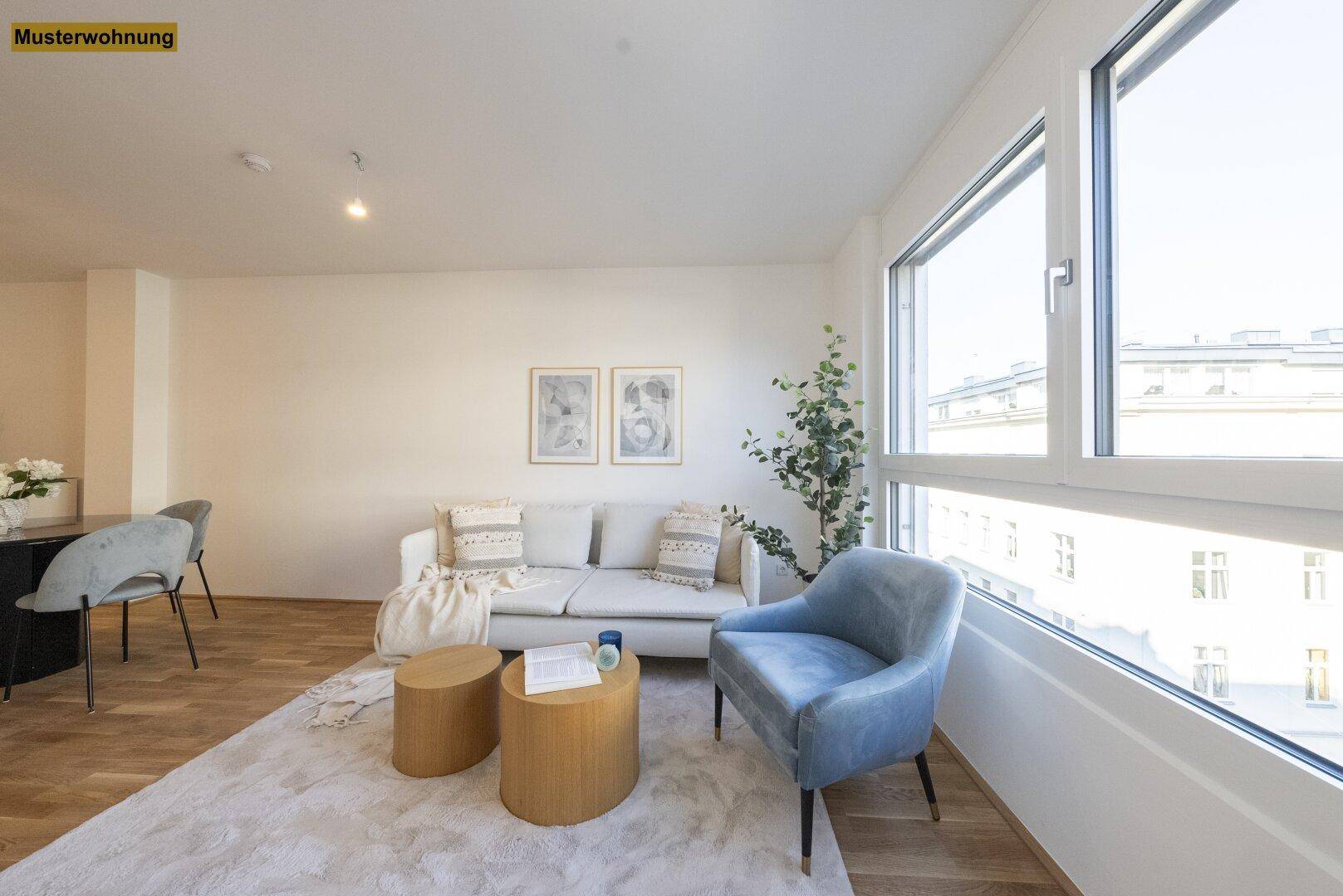 Heller Wohnbereich mit beigem Sofa, blauem Sessel und großen Fenstern mit Stadtblick.