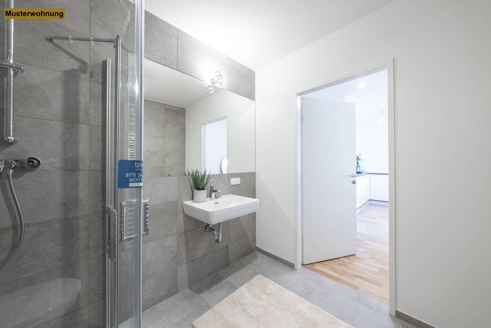 Modernes Badezimmer mit grauen Fliesen, Duschkabine und Zugang zu einem anderen Raum.