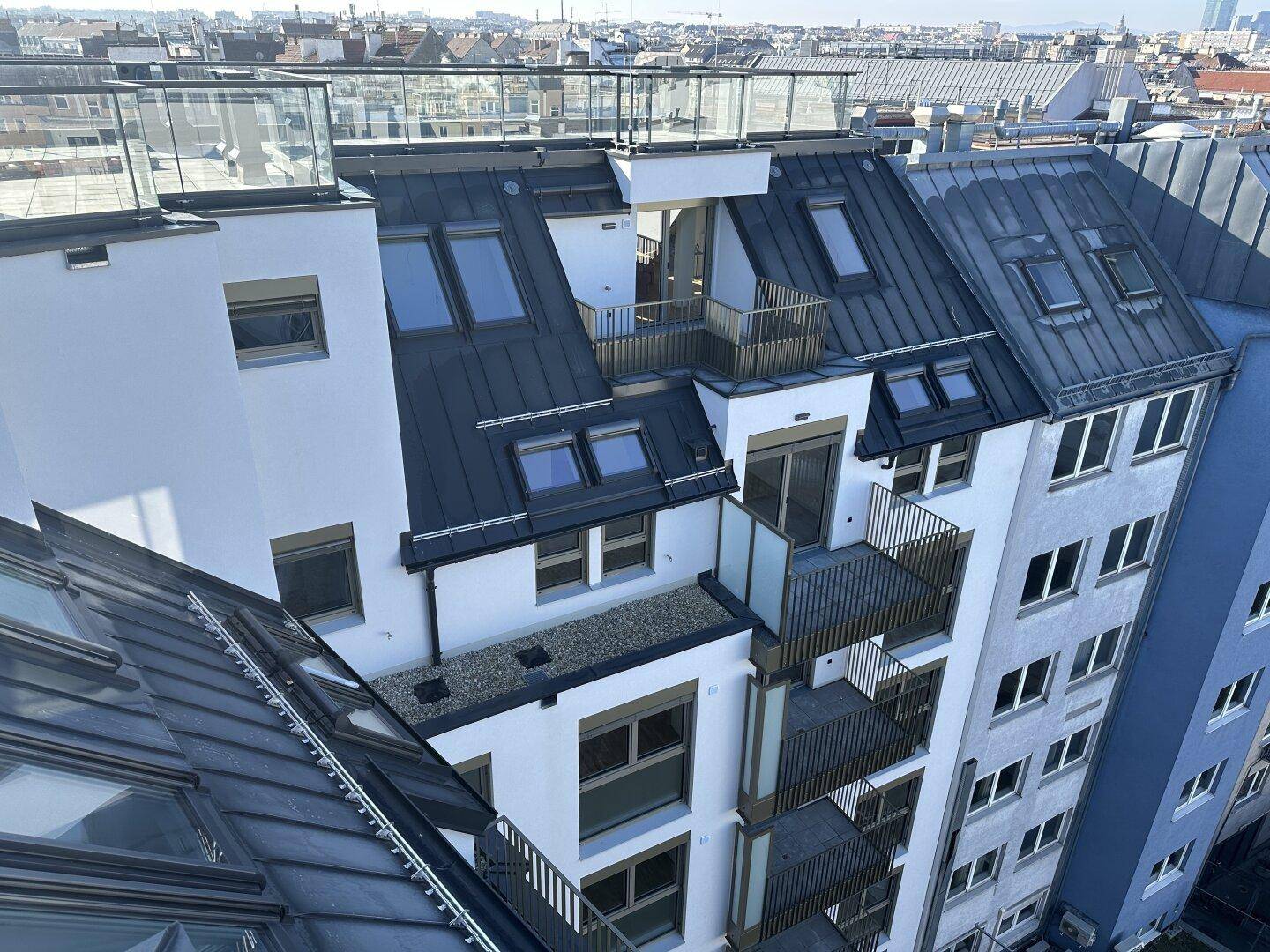 Dachansicht eines modernen Wohngebäudes mit mehreren Balkonen und Blick über die Stadt.