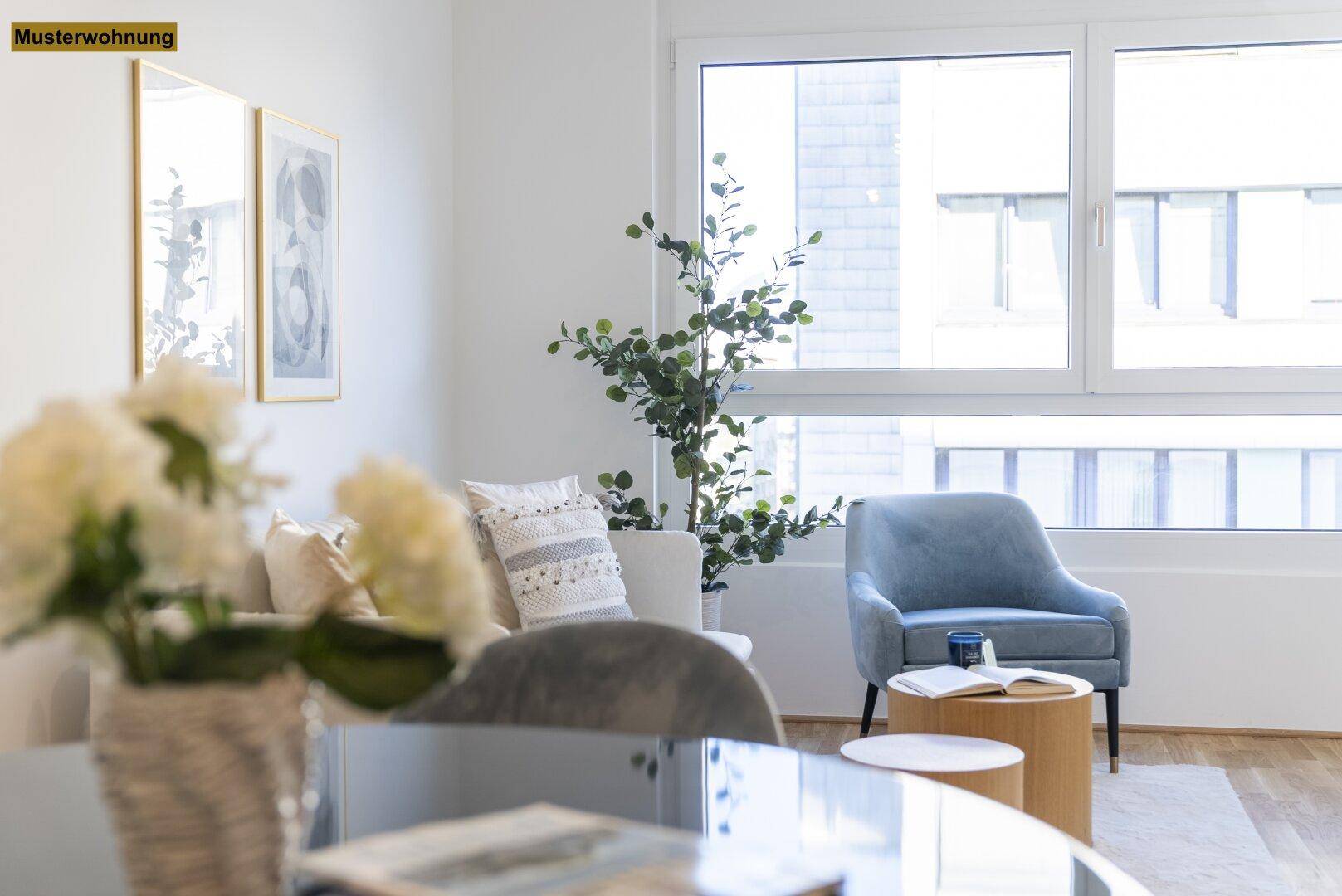 Helles Wohnzimmer mit beigem Sofa, blauem Sessel und großen Fenstern, die viel Tageslicht hereinlassen.