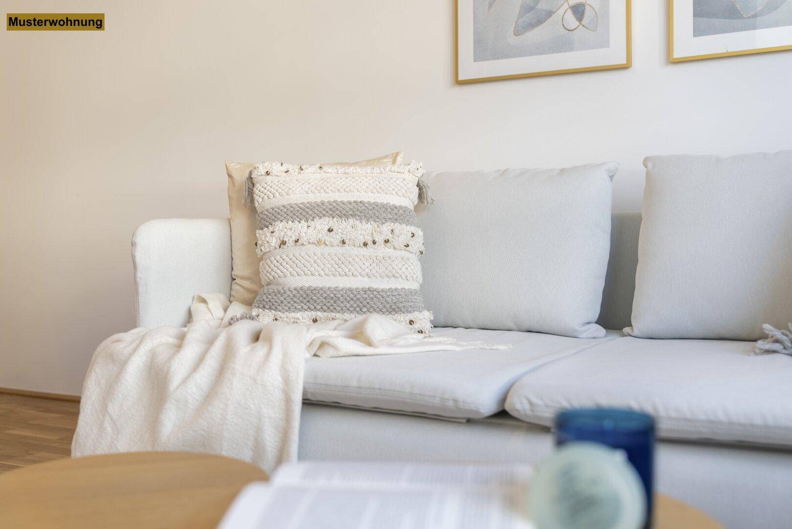 Detailansicht eines beigen Sofas mit strukturierten Kissen und einer weichen Decke in einem hellen Wohnzimmer.