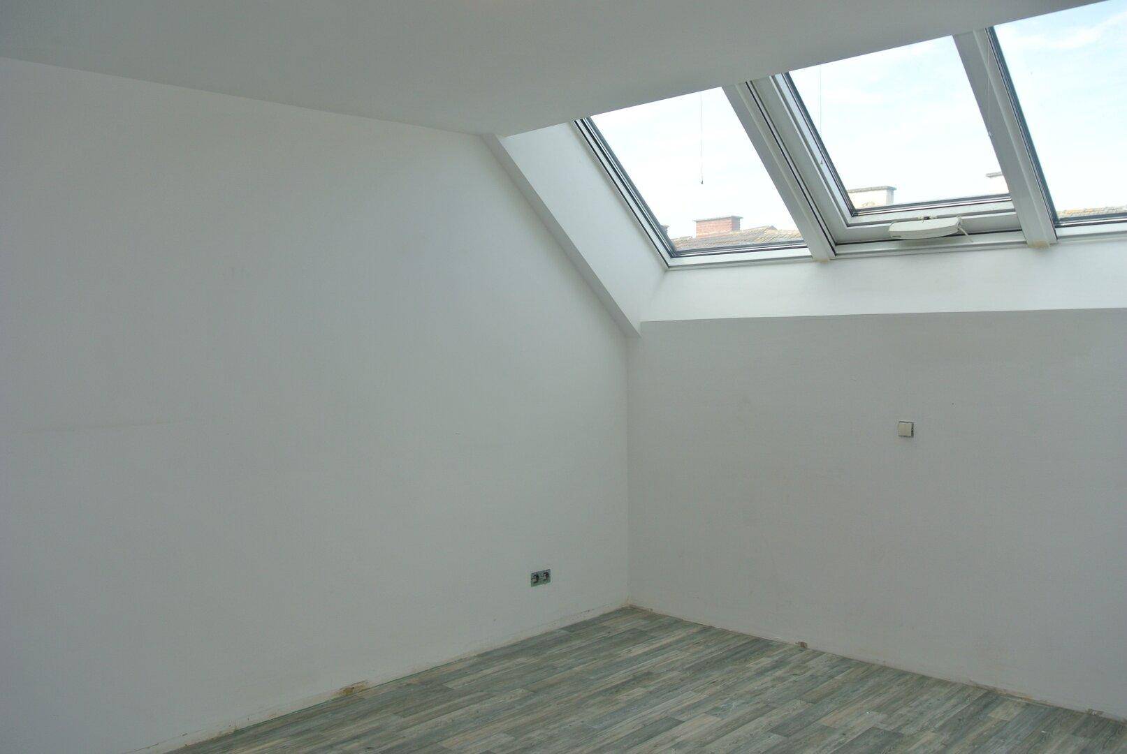 Heller Dachbodenraum mit schrägen Wänden, Holzboden und großen Dachfenstern.