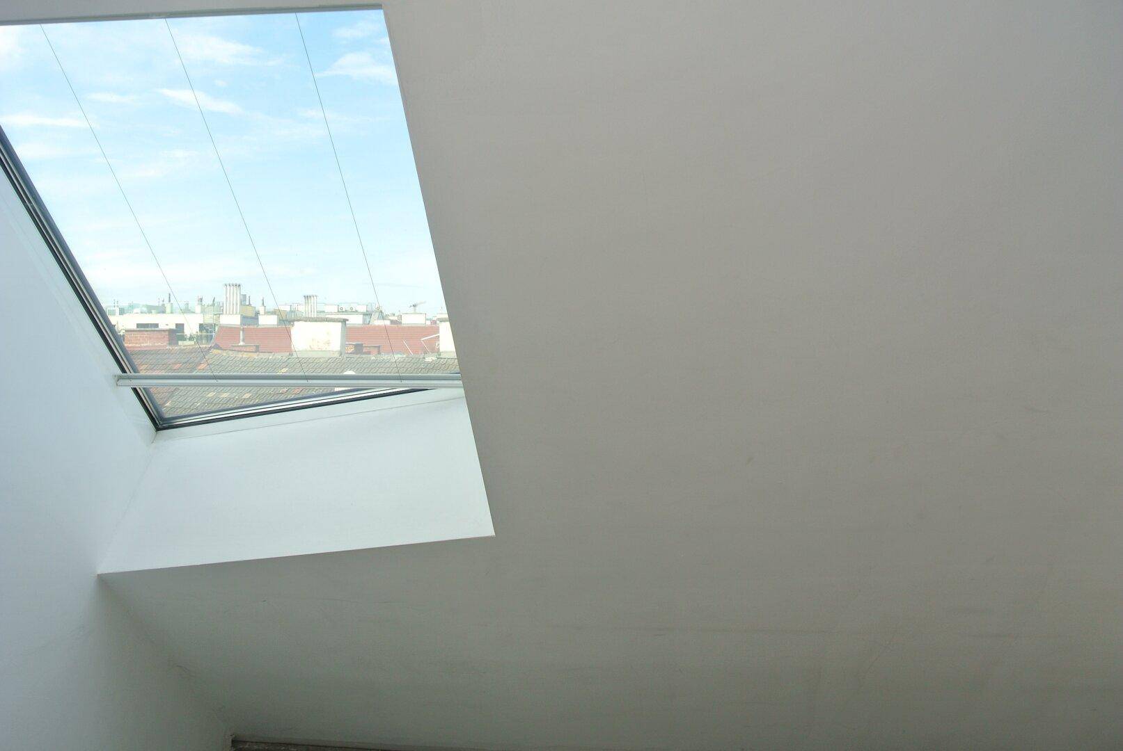 Helle Wand mit einem einzelnen Dachfenster, das einen Blick auf den Himmel bietet.