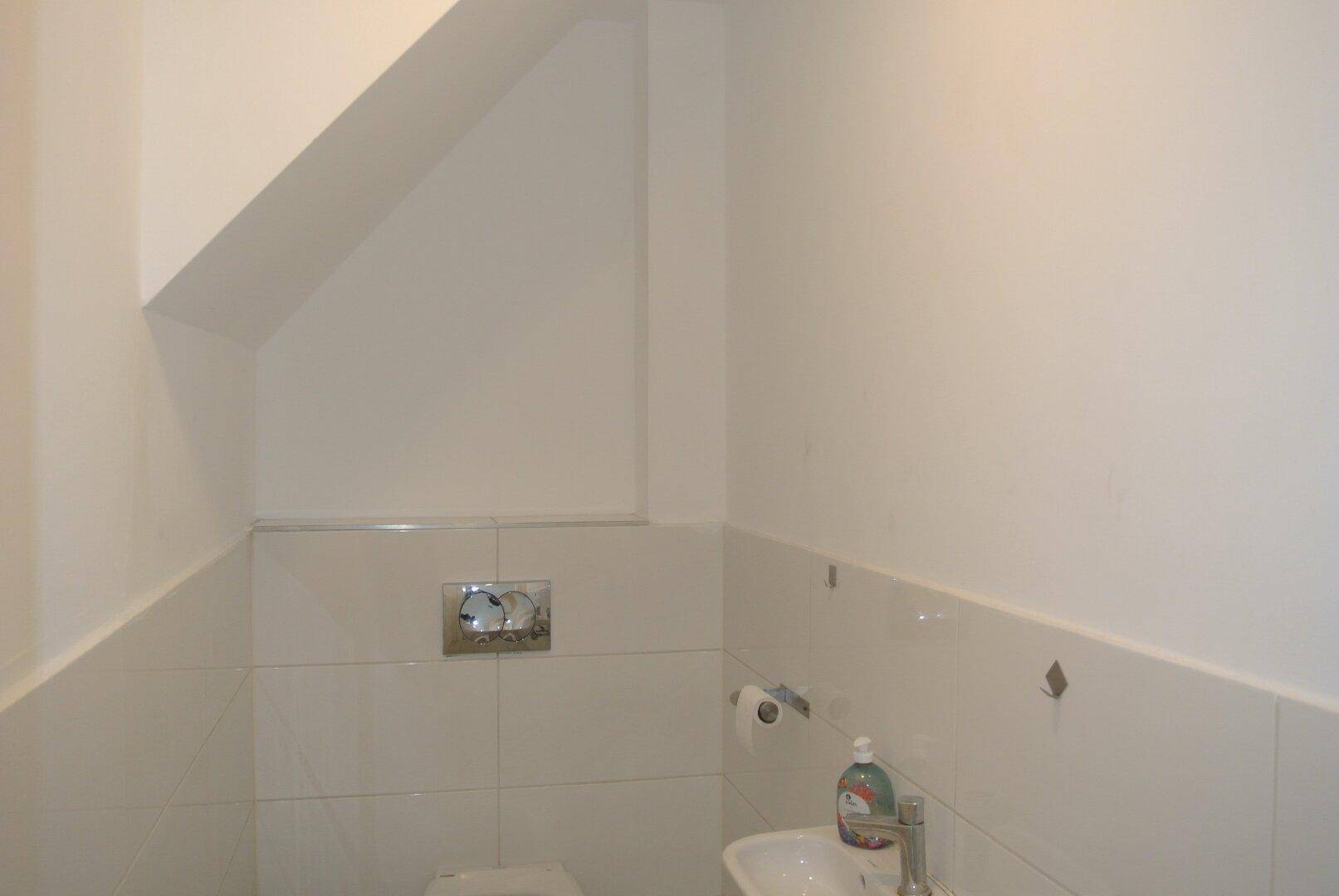Kleines Gäste-WC mit weißen Fliesen, wandmontierter Toilette und Waschbecken.