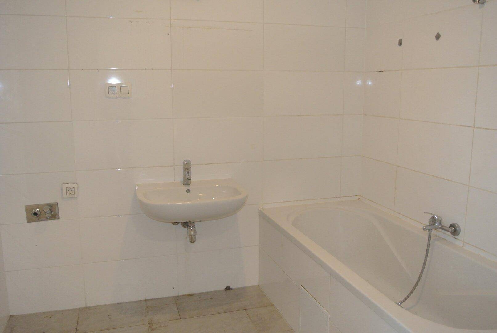 Einfaches Badezimmer mit weißen Fliesen, Waschbecken und einer Badewanne.