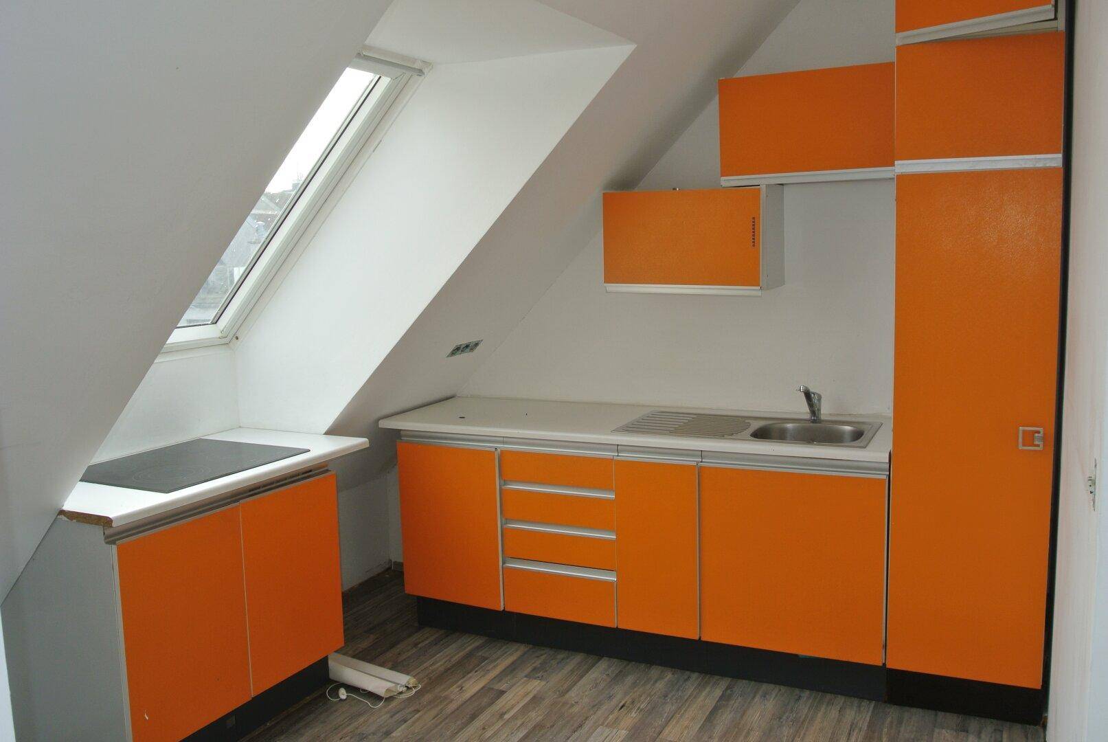 Küche im Dachgeschoss mit orangefarbenen Schränken, Dachfenster und Kochfeld.