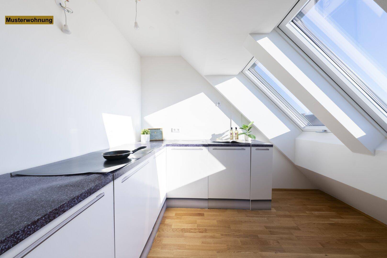 Helle Küche mit minimalistischen weißen Schränken, dunkler Arbeitsplatte und viel Tageslicht durch Dachfenster.