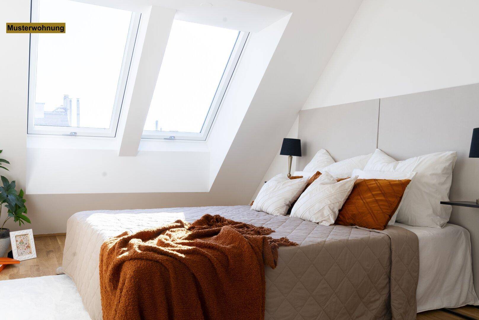 Gemütliches Schlafzimmer mit großem Bett, warmen Textilien und viel Tageslicht durch Dachfenster.