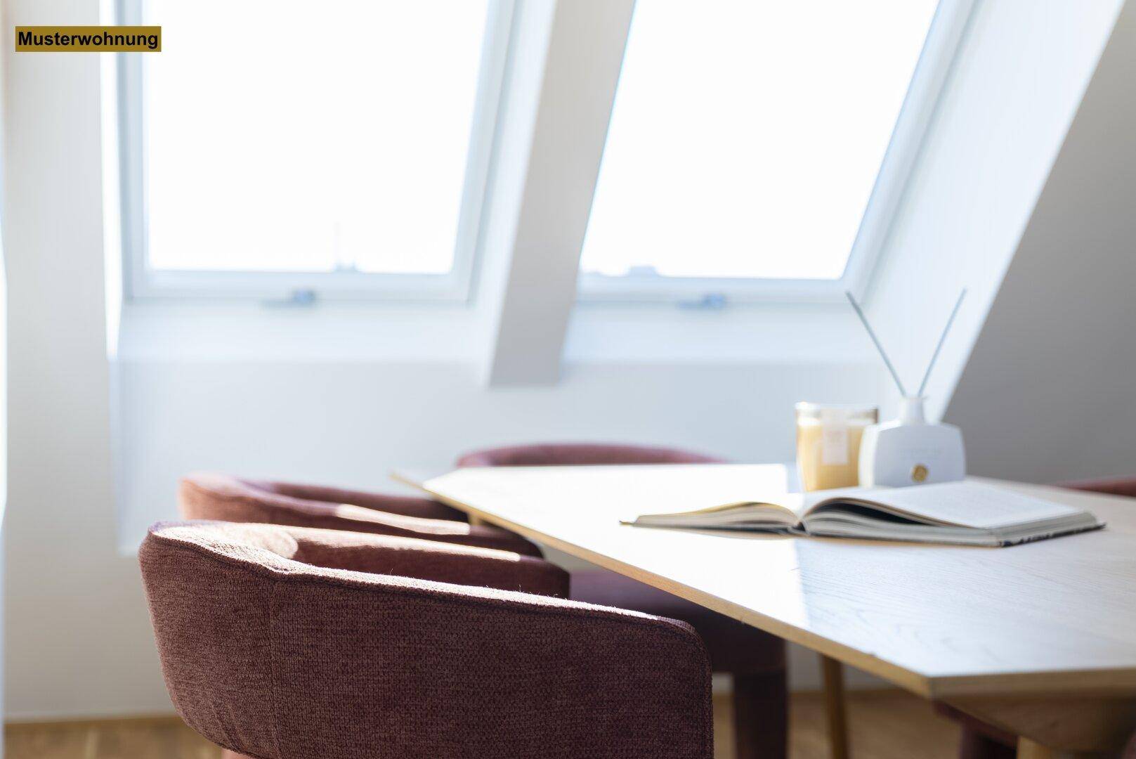 Detailaufnahme eines Esstisches mit Buch und Dekoration, im Hintergrund helle Dachfenster.